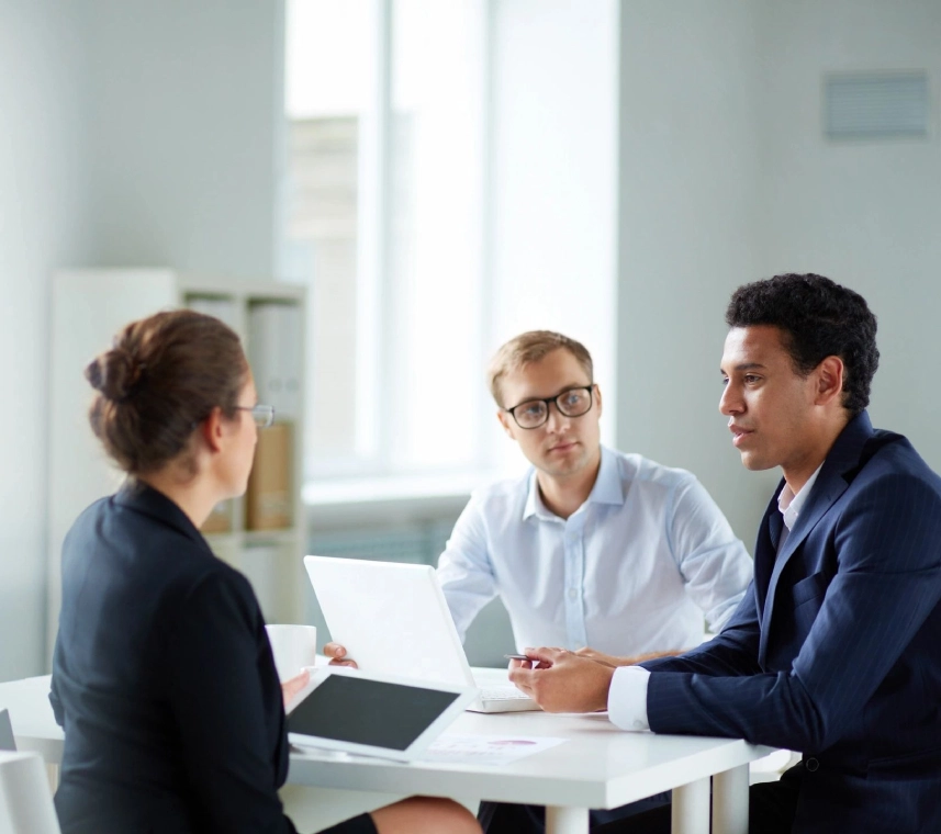 Three people sitting at a table with papers and laptops.