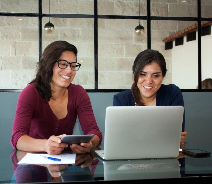 Two women sitting at a table looking at a laptop.